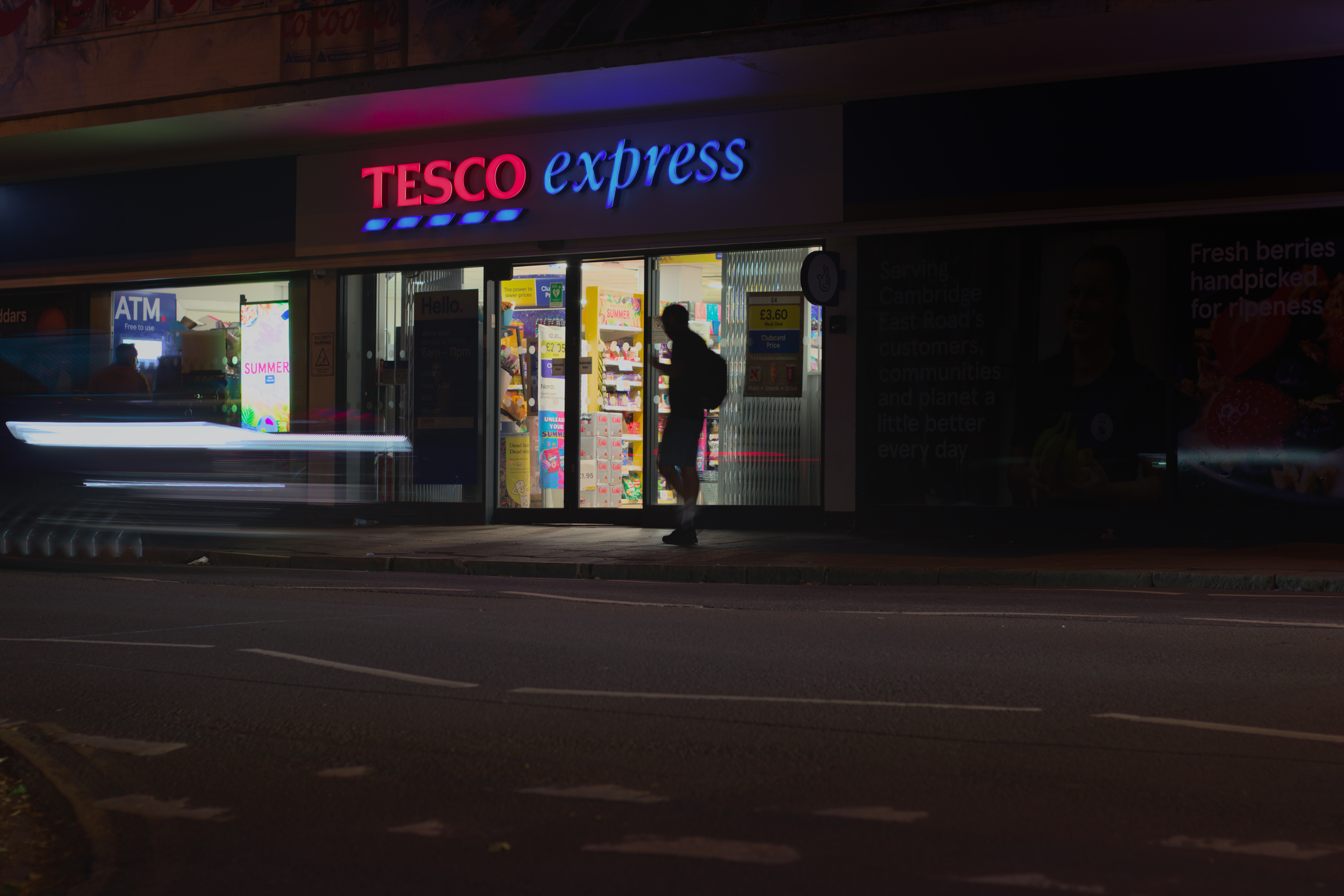A silhouette walks in front of a bright supermarket doorway on a dark street