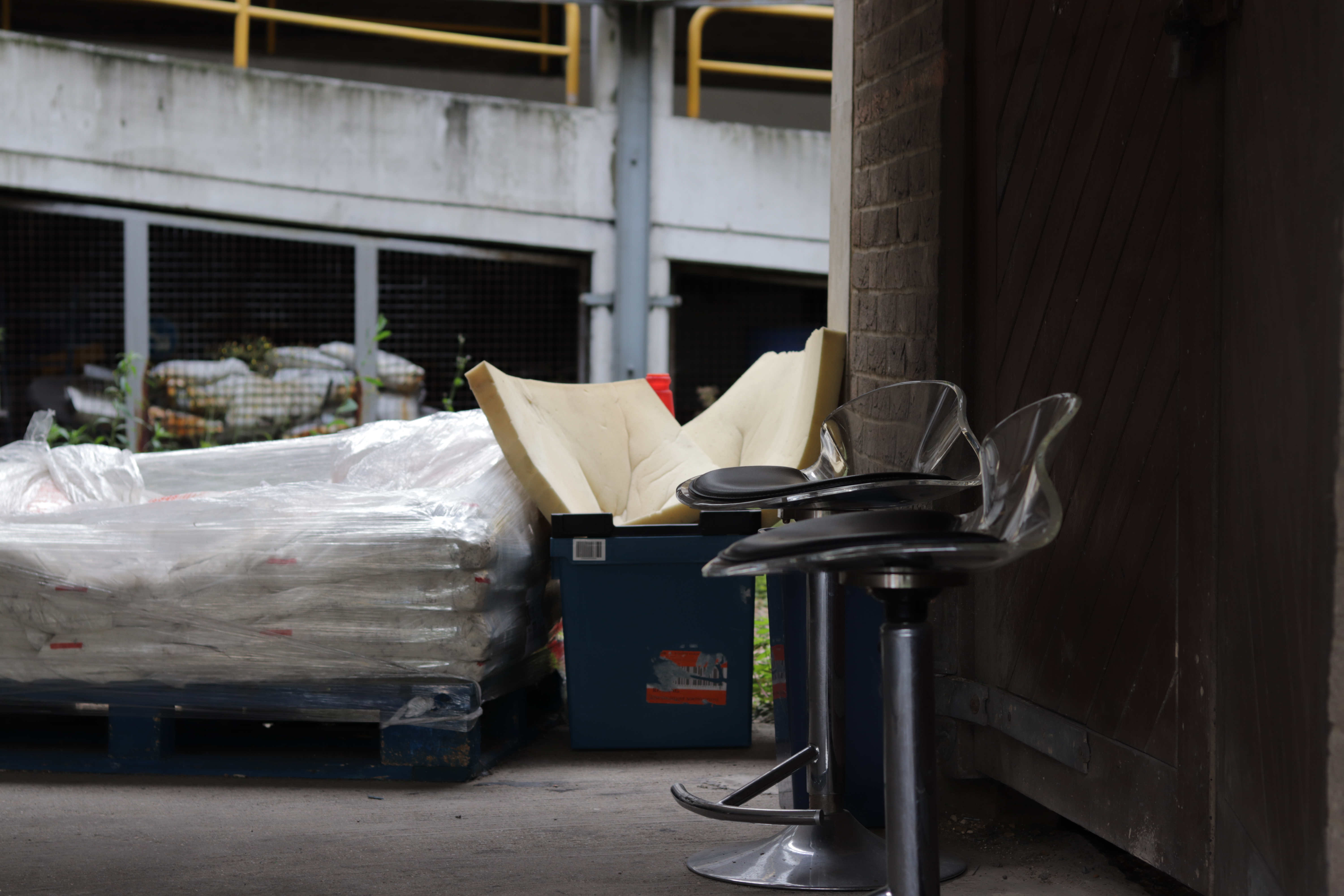 two bar stools in shadow in front of some sunlit garbage with a parking lot in the background