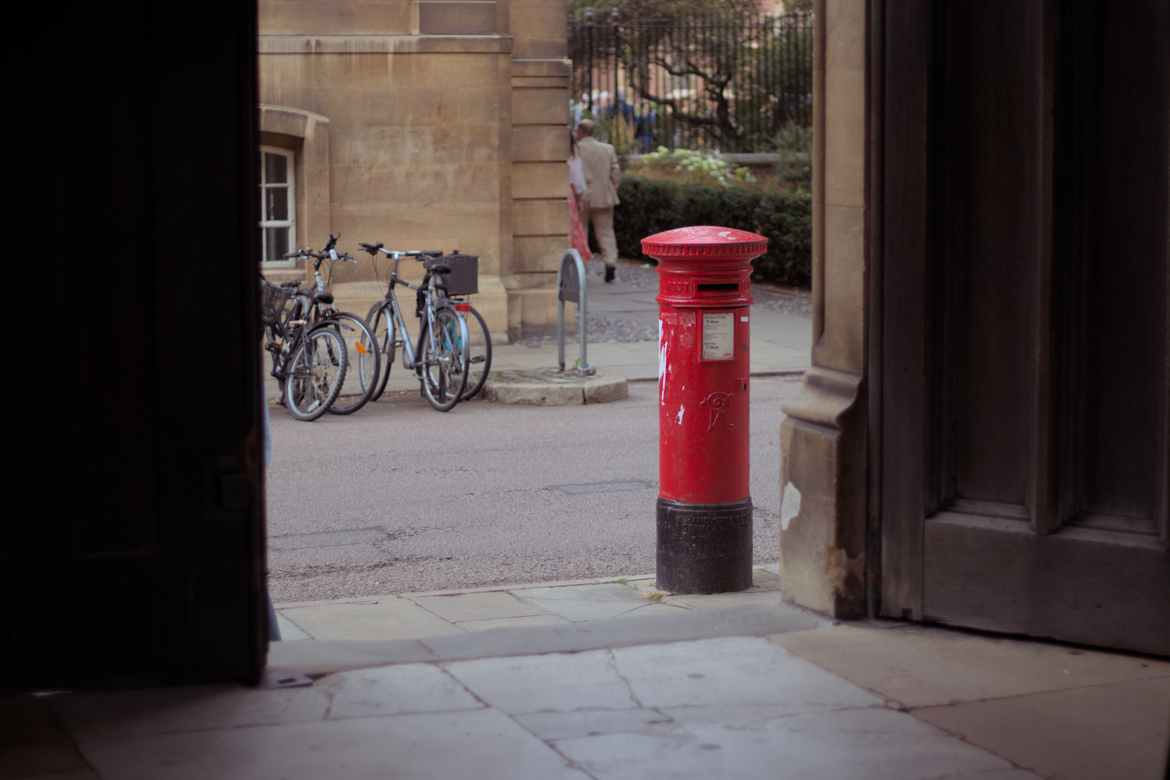 A post box viewed through a huge doorway with old wooden doors, bicycles parked in background
