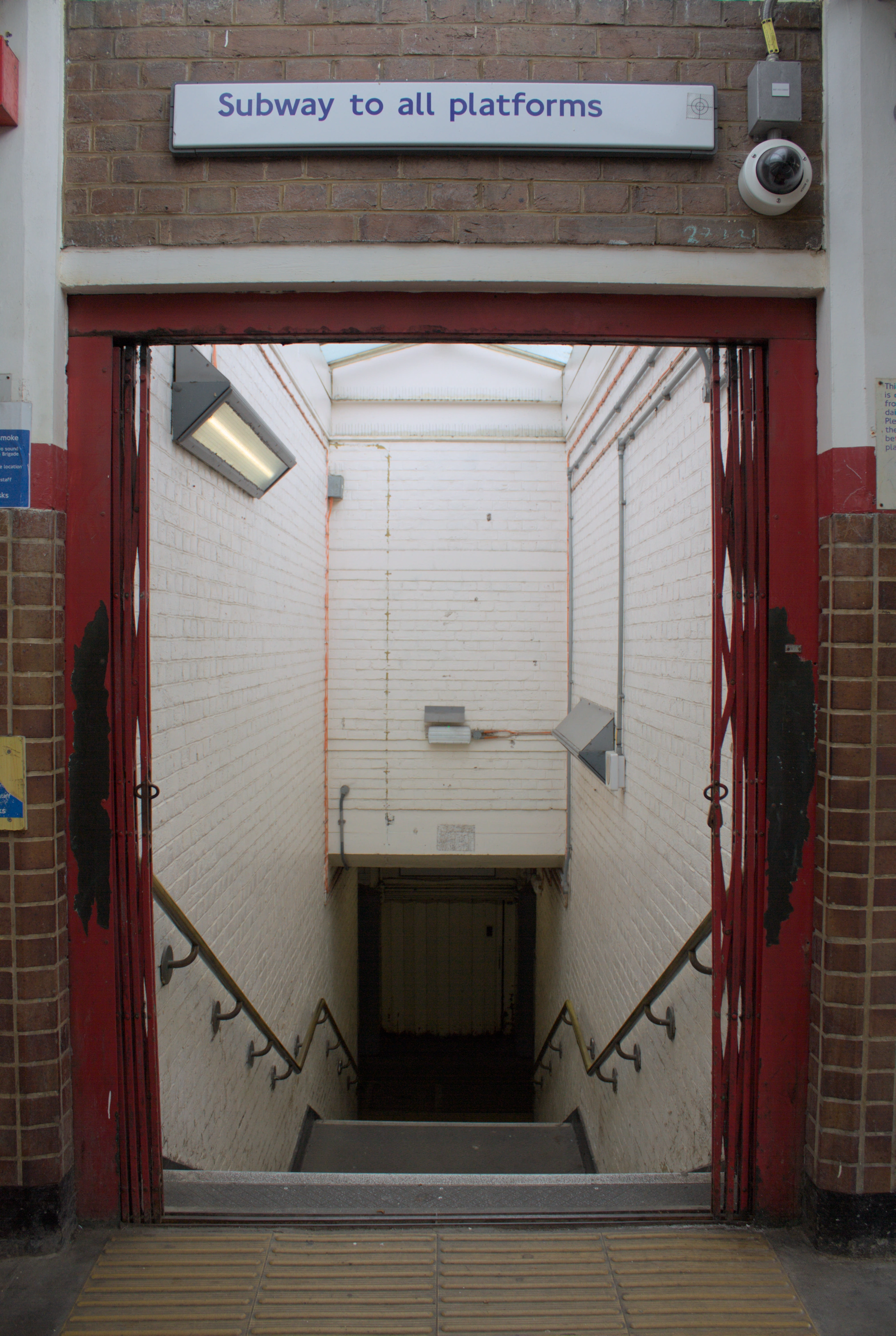 A photo of stairs on a station platform, heading downwards, with a red doorframe