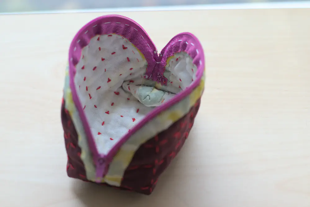 a zippered pouch with contrasting purple and green fabric, and a grid of red stitching