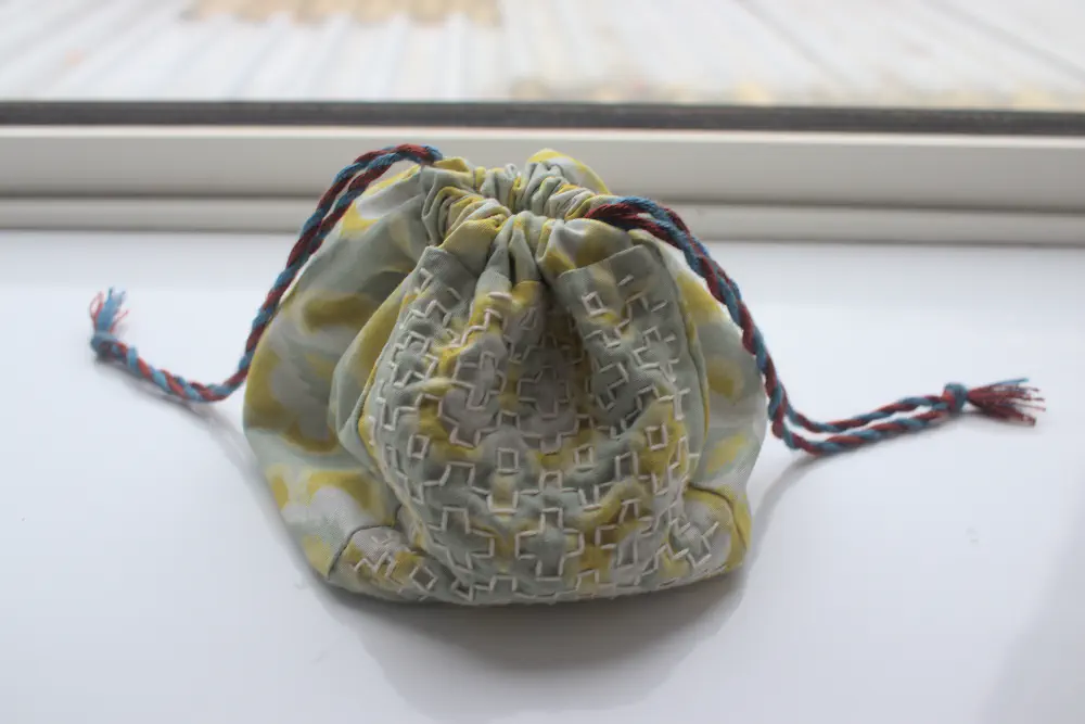 a square drawstring bag with green flowery fabric and blue and red twisted drawstrings