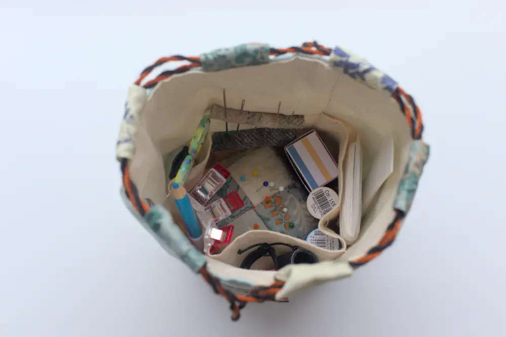 the inside of the bag is made of canvas and has various tools like needles, scissors, thimbles, a hera marker, pincushion
