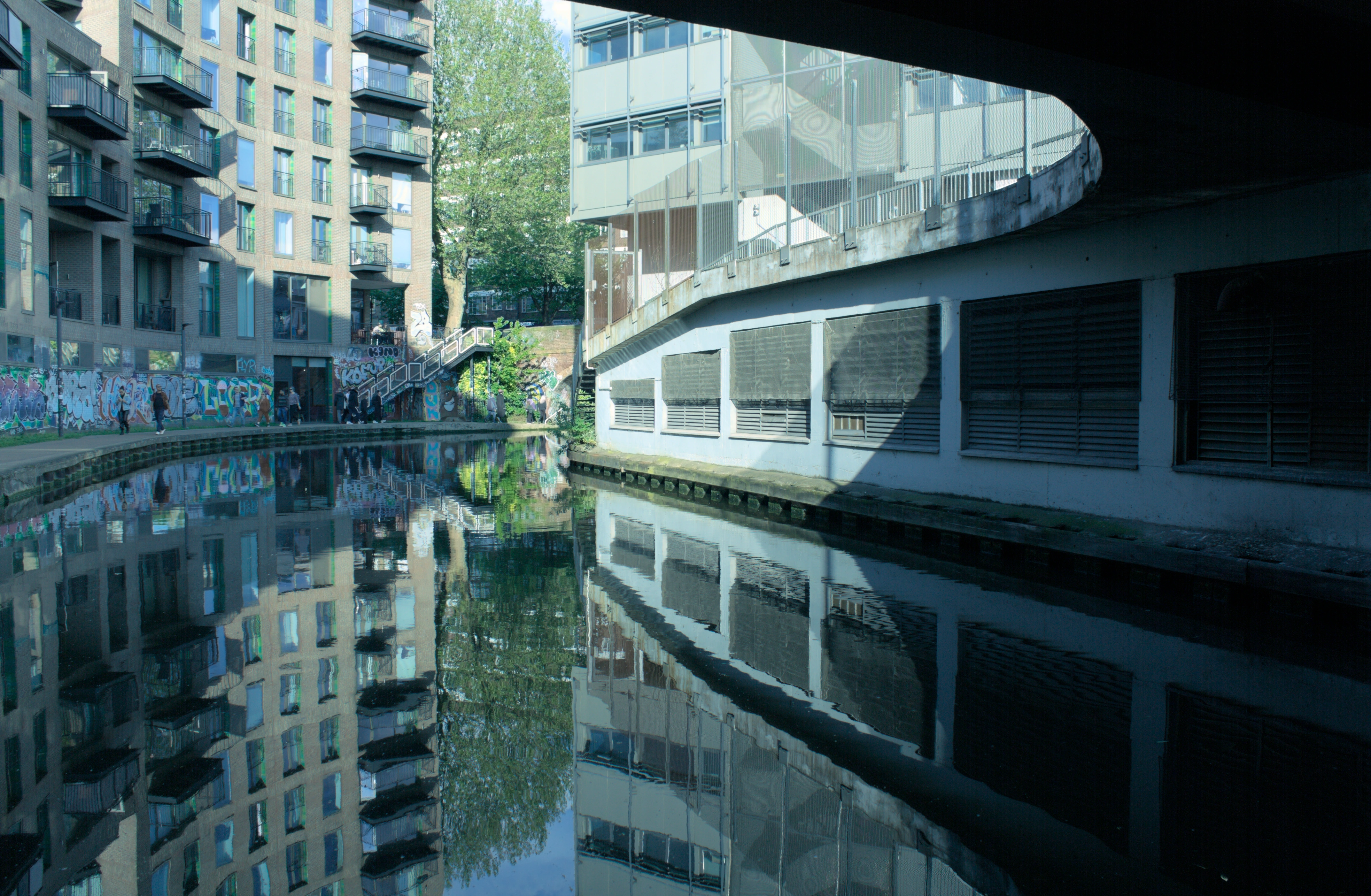 A view of a curve in a canal from under a curved bridge which reflects in the water