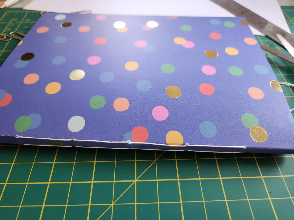 A notebook showing the spine which is flat and has a line of stitches along each of its long edges