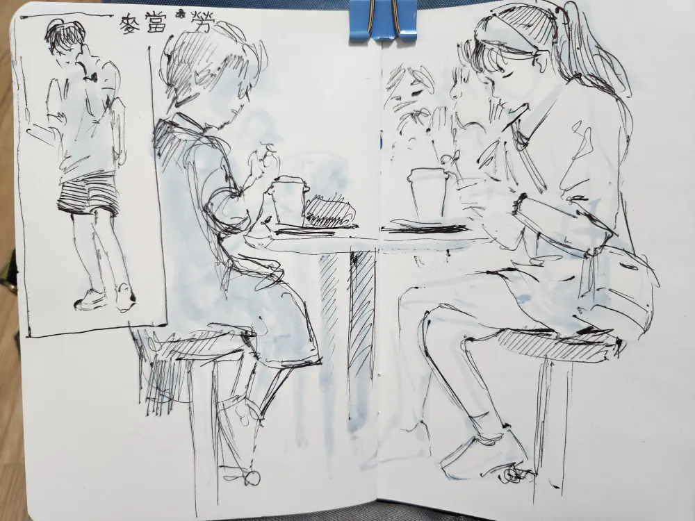 A sketchbook spread in ballpoint and ink wash with a man on his phone on the subway and four women eating mcdonalds