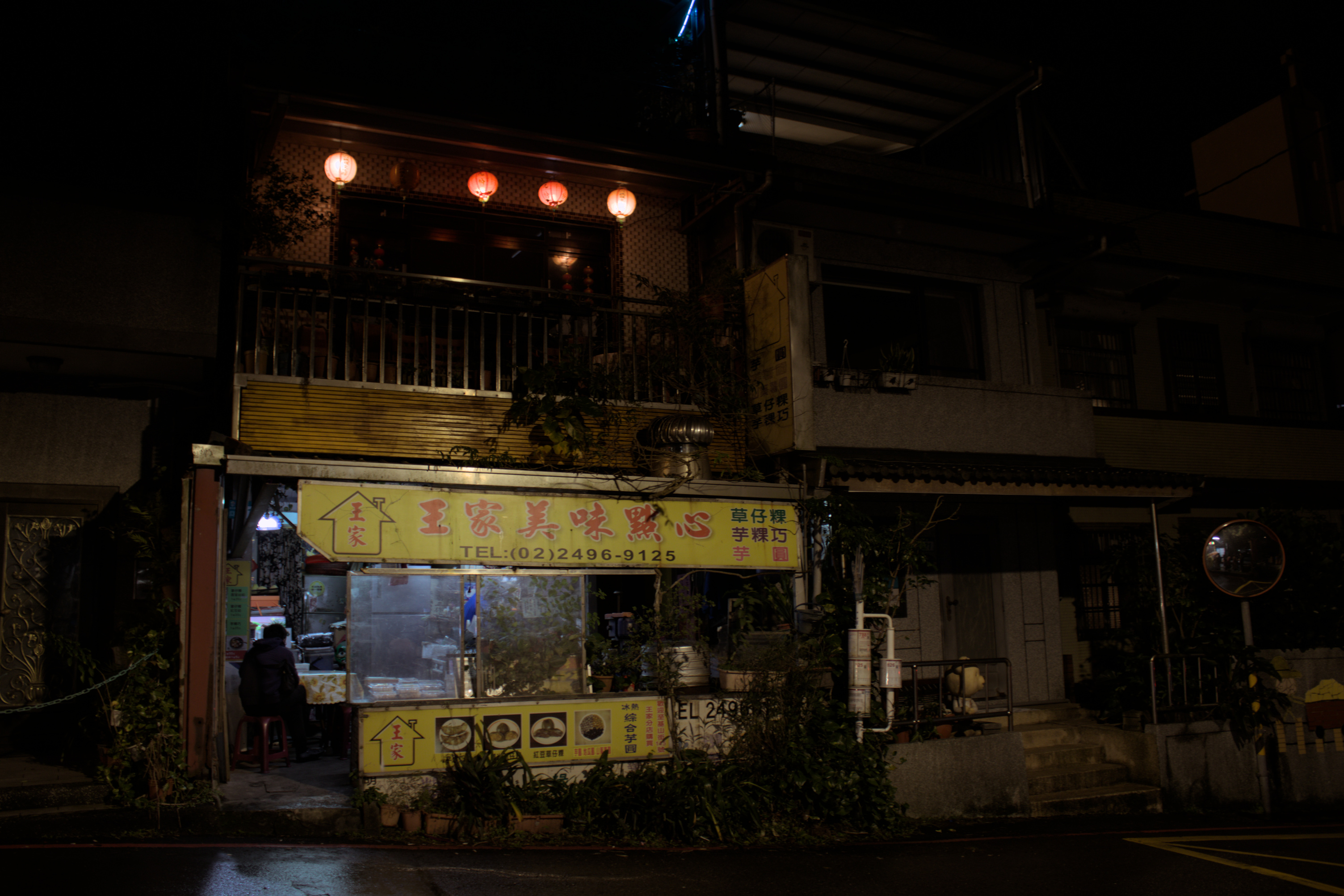 a shopkeeper sitting at a traditional dessert shop at night