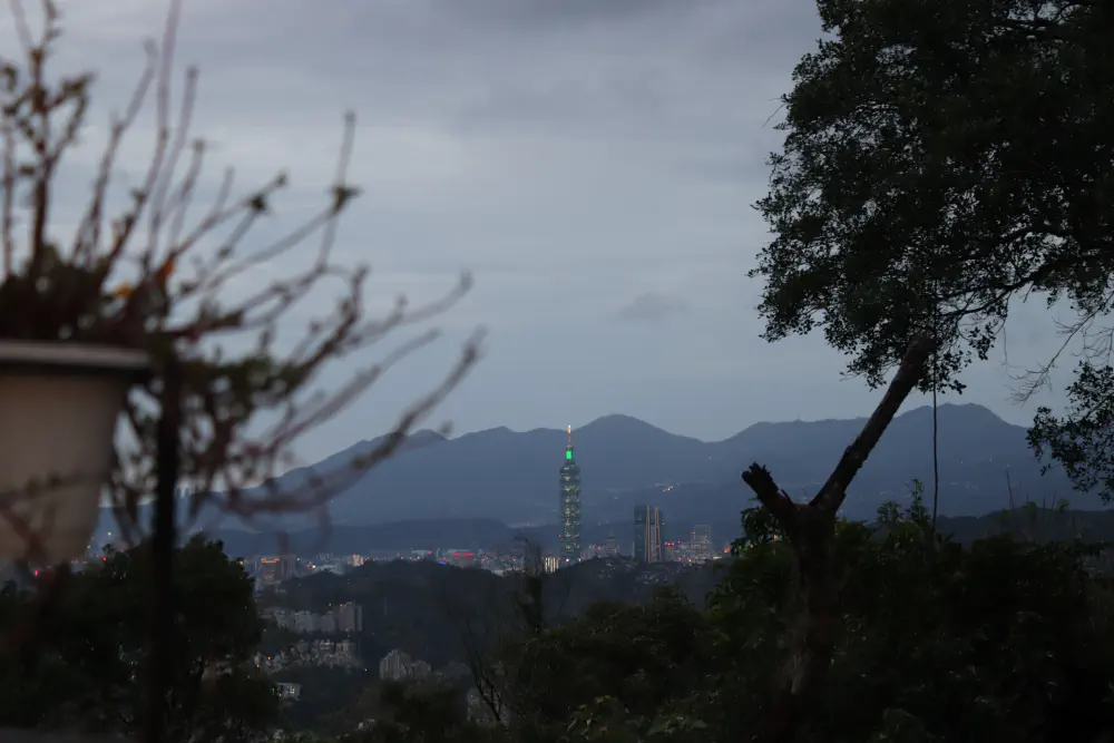 a photo of the skyscraper taipei 101 sticking up from a city surrounded by mountains, at dusk