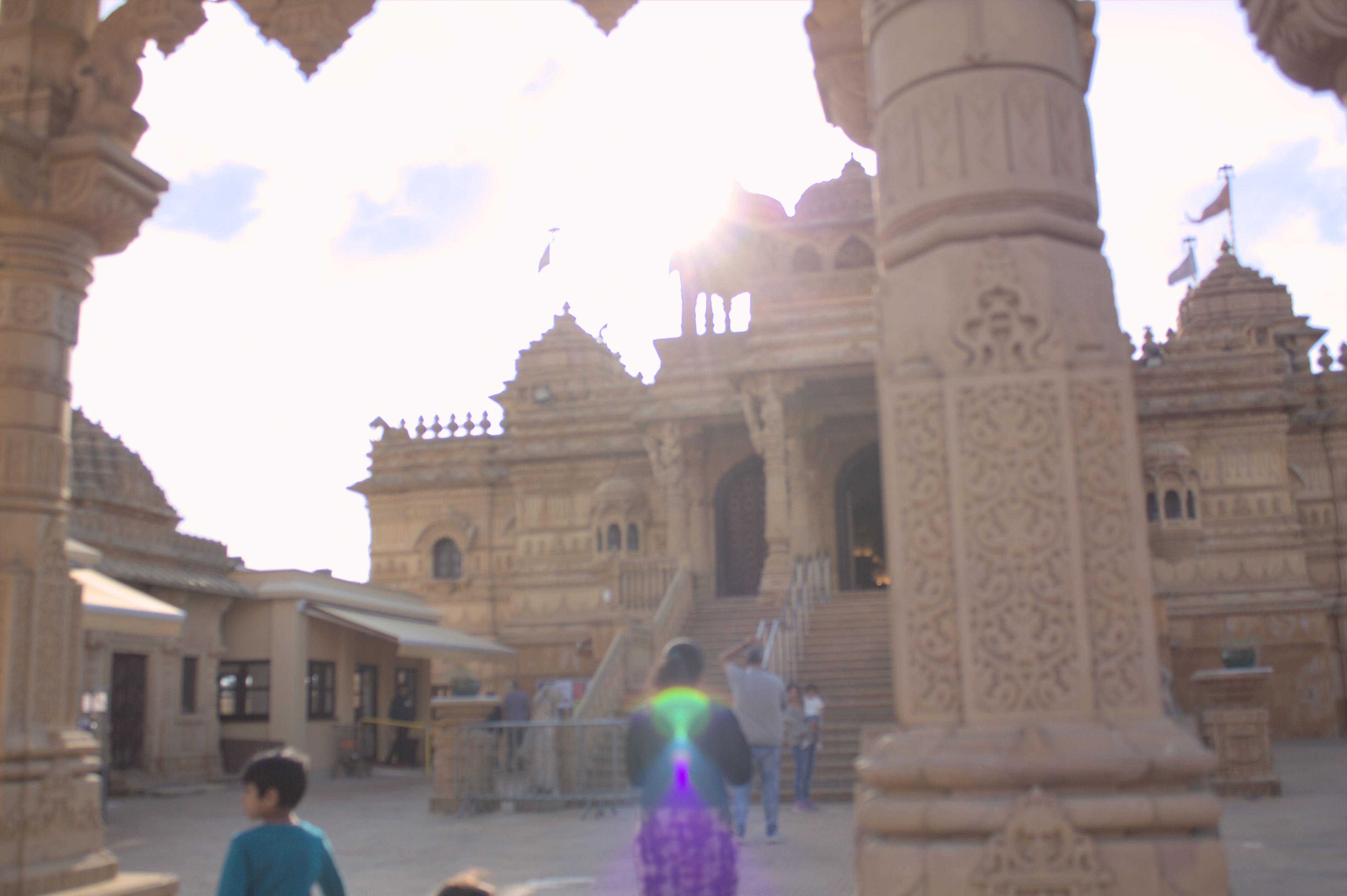 A temple the same cream colour all over, with ornate carvings, multiple pointed rooves and the pillars of the entrance in the foreground